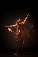 Image showing Young beautiful dancer in beige dress dancing on black background