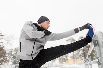 Image showing sports man stretching leg at fence in winter