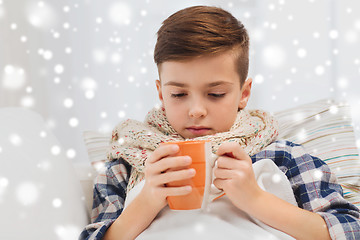 Image showing ill boy with flu in scarf drinking tea at home