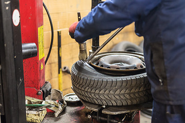 Image showing Professional auto mechanic replacing tire on wheel in car repair service.