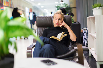 Image showing Charming girl sitting by wooden table and reading book