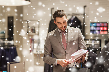 Image showing happy young man choosing shirt in clothing store