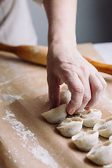 Image showing woman folds the raw dumplings on a sheet of parchment