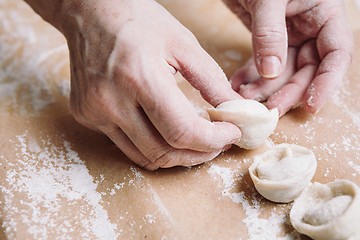 Image showing woman folds the raw dumplings on a sheet of parchment