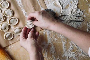 Image showing woman folds the raw dumplings on a sheet of parchment