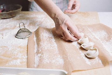 Image showing woman folds the raw dumplings on a sheet of parchment