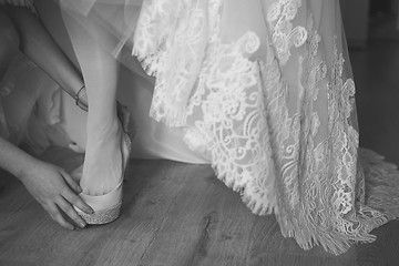 Image showing bridesmaid helping bride to put on elegant shoes. Black and white shot