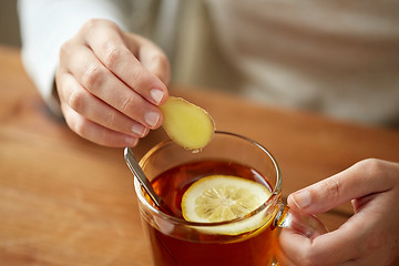 Image showing close up of woman adding ginger to tea with lemon