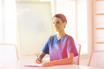 Image showing happy female doctor or nurse writing to clipboard