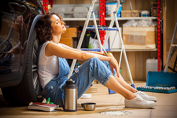 Image showing auto mechanic woman in blue overalls resting near the wheel of t