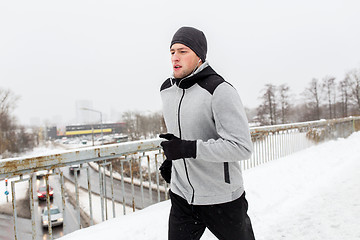 Image showing man in earphones running along winter bridge