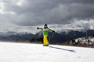 Image showing Happy young skier with ski poles in sun mountains and cloudy gra