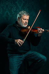 Image showing Senior musician playing a violin with wand on black background