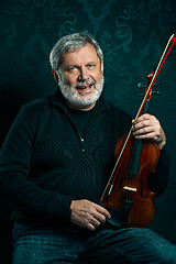 Image showing Senior musician playing a violin with wand on black background