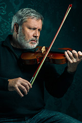 Image showing Senior musician playing a violin with wand on black background