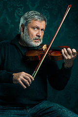 Image showing Senior musician playing a violin with wand on black background