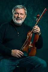 Image showing Senior musician playing a violin with wand on black background