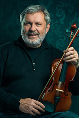 Image showing Senior musician playing a violin with wand on black background