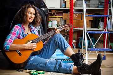 Image showing beautiful Woman mechanic in blue overalls resting with a guitar