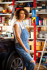 Image showing curly-haired woman in blue overalls mechanic near a car 