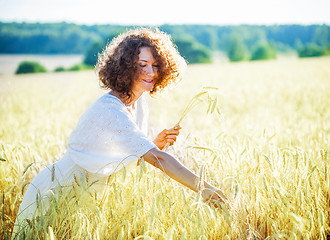 Image showing smiling woman in a light dress collects in the ears of the field