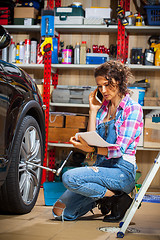 Image showing car mechanic woman in blue overalls talking on the phone near a 