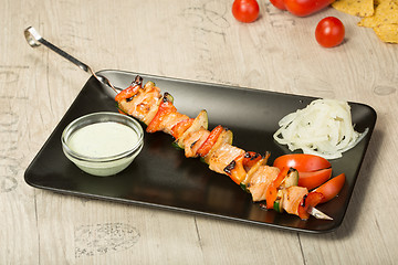 Image showing shashlik. kebab skewer, black rectangular plate. sauce and onions