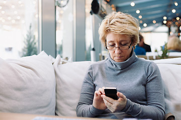 Image showing Mid age woman with cell phone sitting cafe