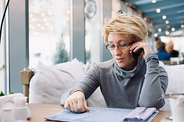 Image showing Mid age woman talking on cell phone sitting cafe