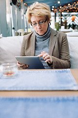 Image showing Mid age woman with tablet sitting cafe