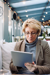 Image showing Mid age woman with tablet sitting cafe