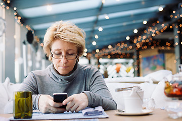 Image showing Mid age woman with cell phone sitting cafe