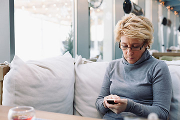 Image showing Mid age woman with cell phone sitting cafe