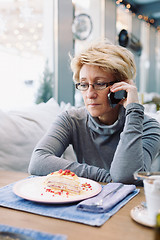 Image showing Mid age woman talking on cell phone sitting cafe