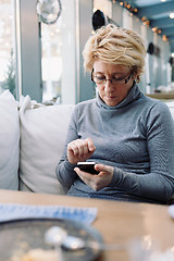 Image showing Mid age woman with cell phone sitting cafe