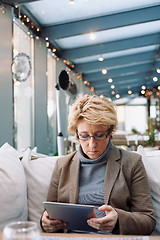 Image showing Mid age woman with tablet sitting cafe