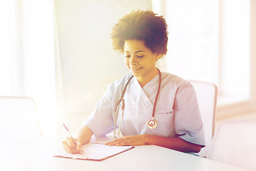 Image showing happy female doctor or nurse writing to clipboard