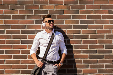 Image showing young man in headphones with bag over brickwall