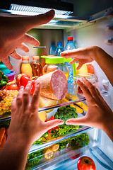 Image showing Human hands reaching for food at night in the open refrigerator