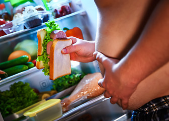 Image showing Hungry man holding a sandwich in his hands and standing next to 