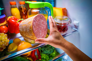 Image showing Human hands reaching for food at night in the open refrigerator