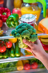 Image showing Woman takes the broccoli from the open refrigerator.