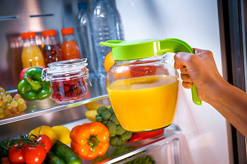 Image showing Woman takes the Orange juice from the open refrigerator