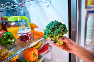 Image showing Woman takes the broccoli from the open refrigerator.