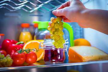 Image showing Woman takes the bunch of grapes from the open refrigerator