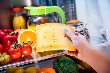 Image showing Woman takes the piece of cheese from the open refrigerator