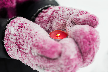 Image showing close up of hands in winter mittens holding candle