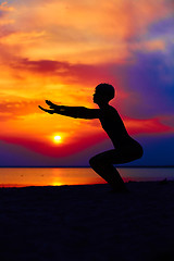 Image showing Silhouette of woman standing at yoga pose on the beach during an amazing sunset