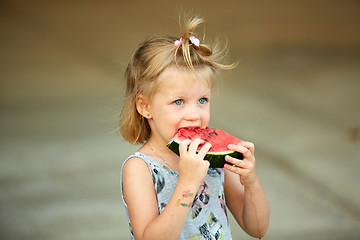 Image showing Adorable blonde girl eats a slice of watermelon outdoors.