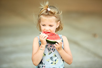 Image showing Adorable blonde girl eats a slice of watermelon outdoors.